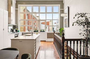 A modern kitchen with a large window, a dining area, and a staircase leading to an upper floor.