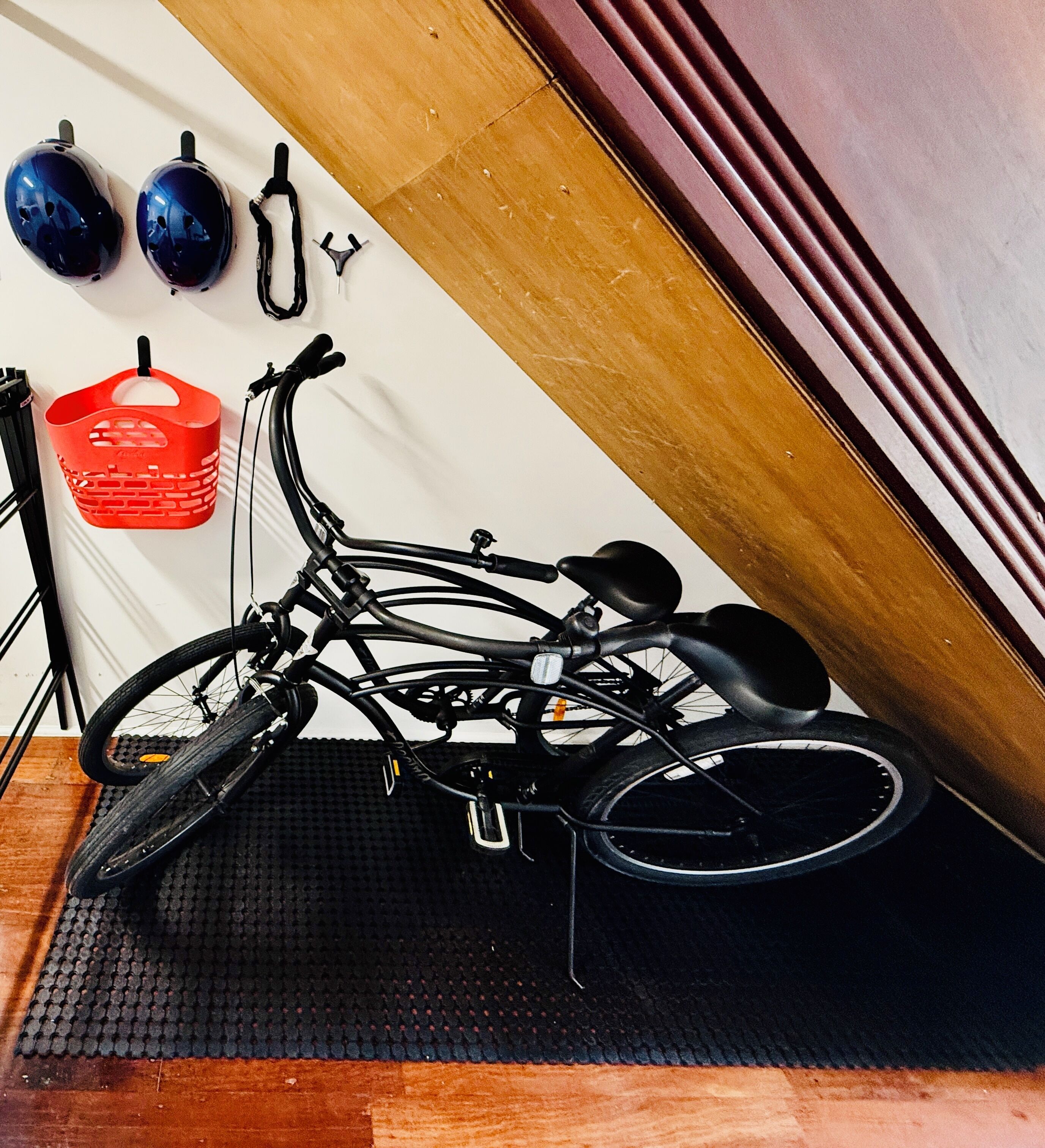 A bicycle leaning against a wall with a red basket hanging on the wall.