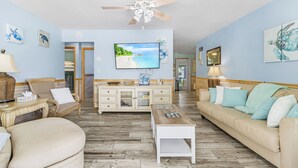 A living room with a television, a ceiling fan, a sofa, a coffee table, and a wooden floor.