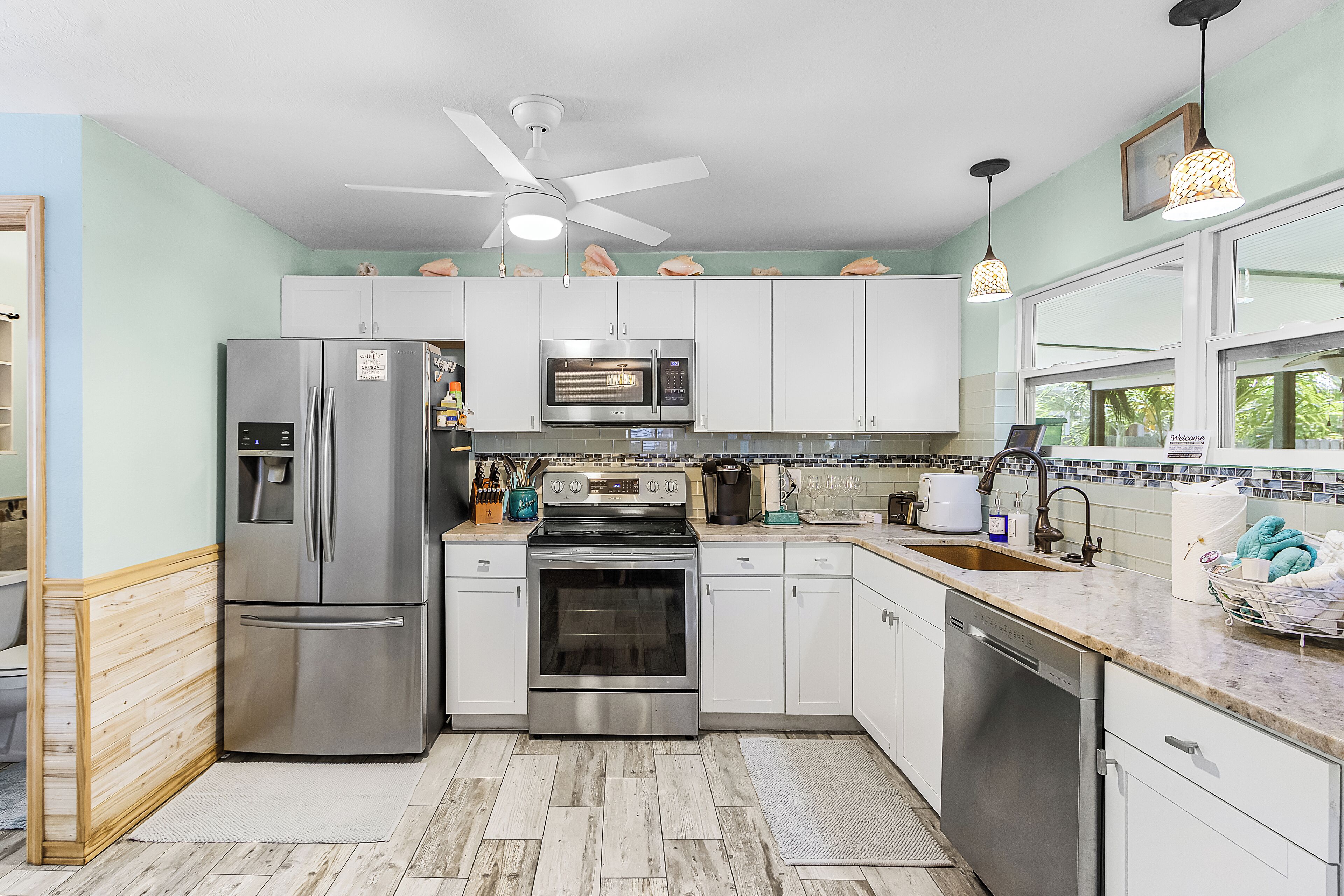 A modern kitchen with stainless steel appliances, white cabinets, a tiled backsplash, and a window with a view.