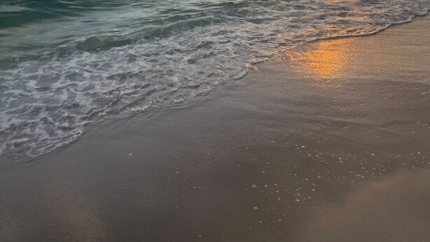 A beach with waves and a sunset.