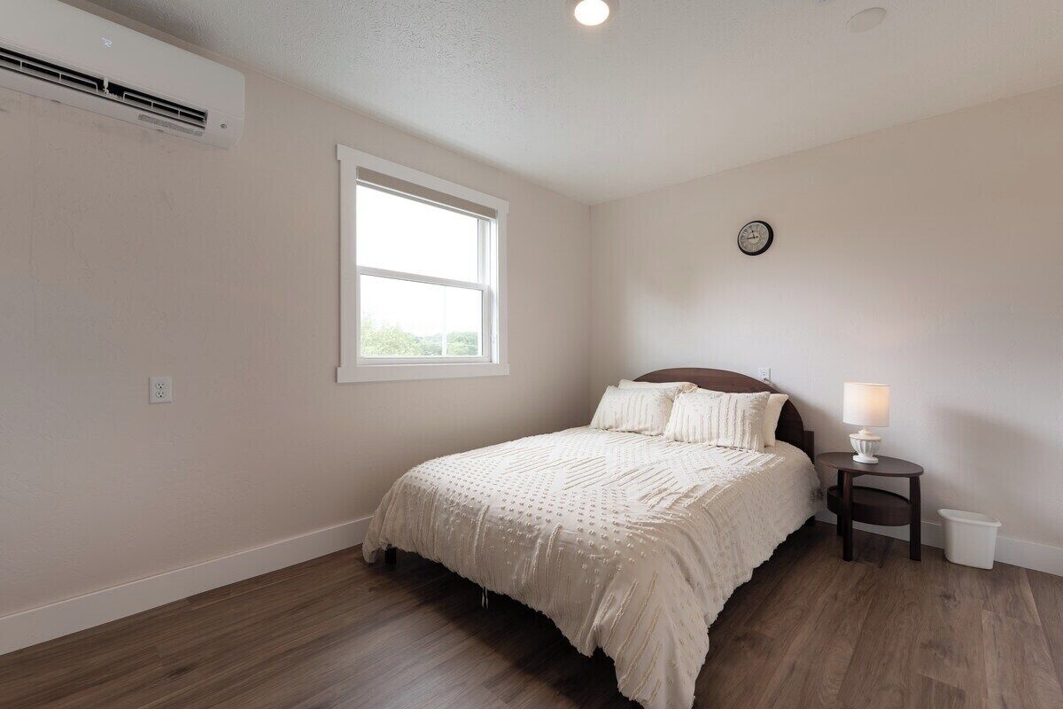 Une chambre à coucher avec un lit, une fenêtre, une horloge murale et une table de chevet avec une lampe.