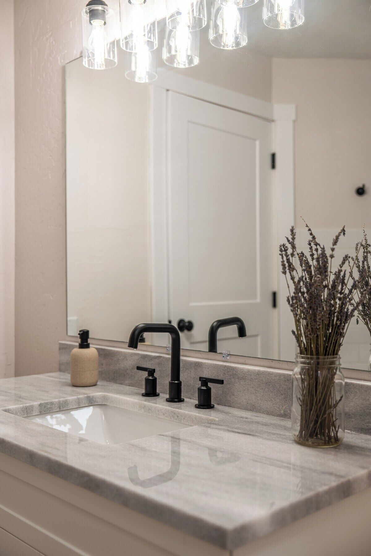 A bathroom with a marble sink, black faucet, and a mirror reflecting a door.