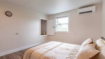 A bedroom with a bed, a window, an air conditioning unit, and a clock on the wall.