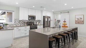 A modern kitchen with white cabinetry, a central island with stools, a microwave, a refrigerator, and a sink. - Old Town-6 BD + Heated Pool + Hot Tub + Game Room (Scottsdale)