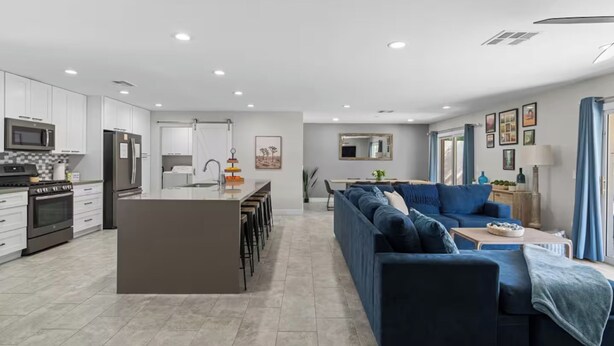 A modern kitchen with white cabinets, a central island, and a dining area with a blue sofa and a coffee table. - Old Town-6 BD + Heated Pool + Hot Tub + Game Room (Scottsdale)