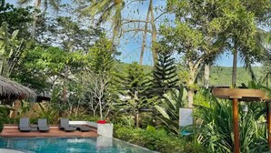 En pool omgivet af palmer og frodig vegetation, med liggestole og et pergola.