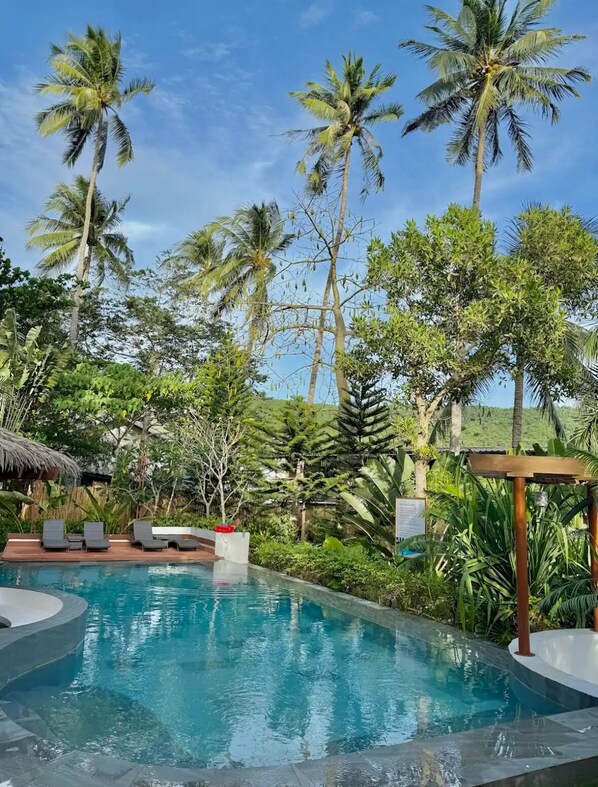 A pool surrounded by palm trees and lush greenery, with lounge chairs and a pergola.