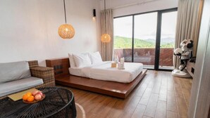 Et moderne hotelværelse med en stor seng, en sofa, et spisebord med frugt og udsigt til det fri.