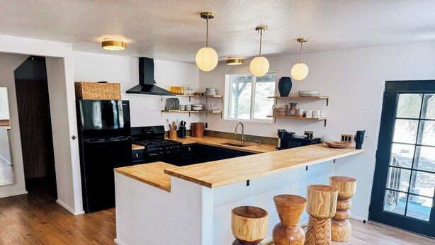 Une cuisine moderne dotée d’un îlot central, de tabourets en bois et de luminaires suspendus.