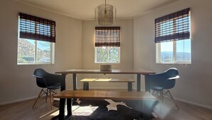 Une pièce comprenant une table à manger en bois, deux chaises, un tapis en peau de vache et un luminaire suspendu.