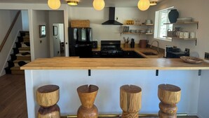 Une cuisine moderne dotée d’un îlot central, de luminaires suspendus et de tabourets en bois.