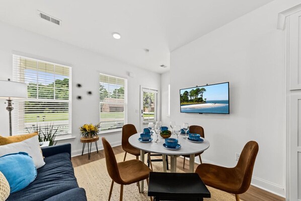 A modern living room with a dining area, white walls, and a TV mounted on the wall.