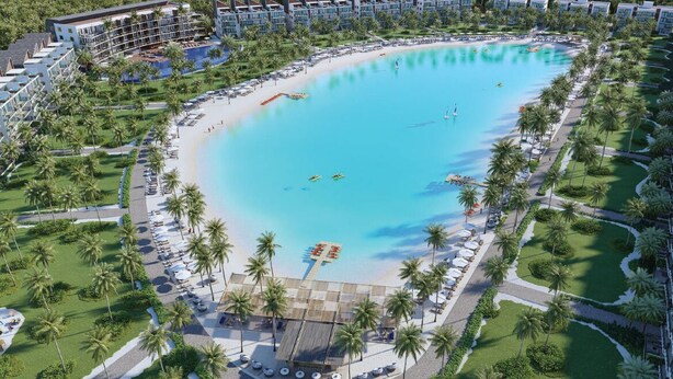 A resort with a large central pool, surrounded by palm trees and a beach area.