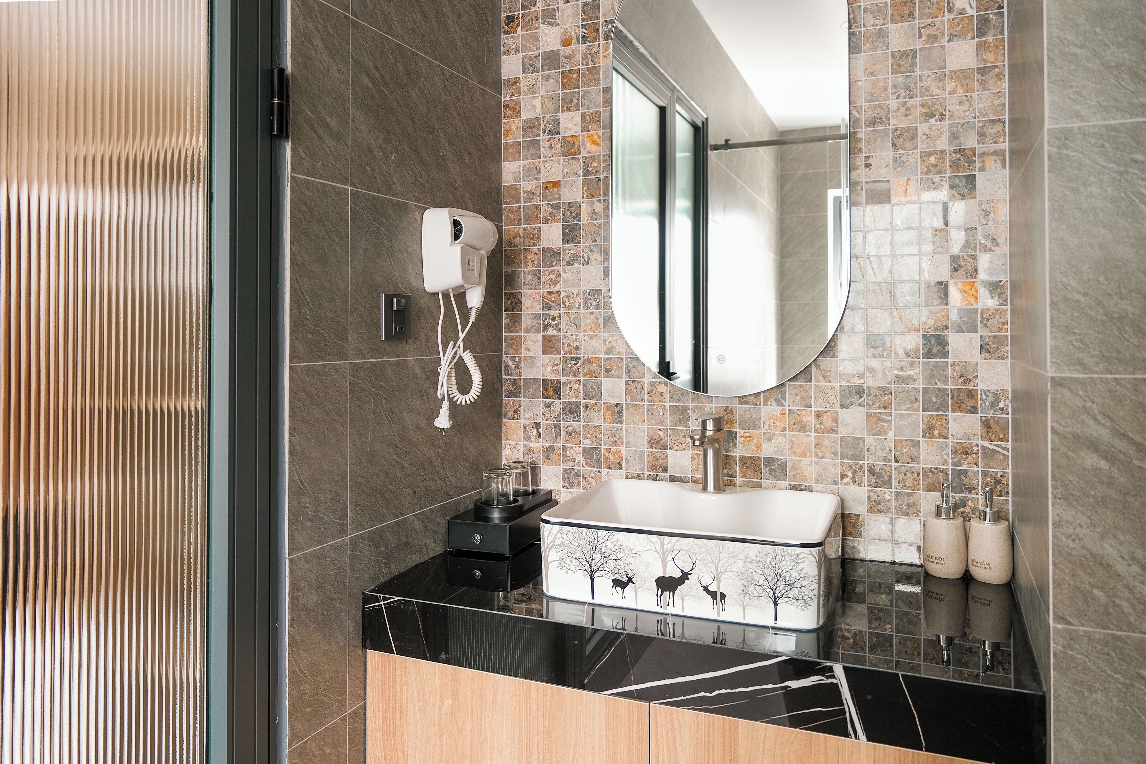 Un baño moderno con encimera negra, lavabo blanco con diseño de ciervo, secador de pelo y espejo.