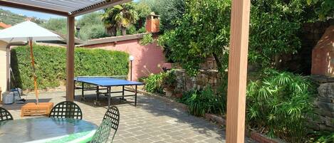 An outdoor patio with a table and chairs, a pergola overhead, and a stone wall with greenery.