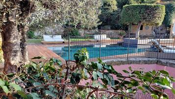 A pool area with a stone wall, a white lounge chair, and a metal fence.