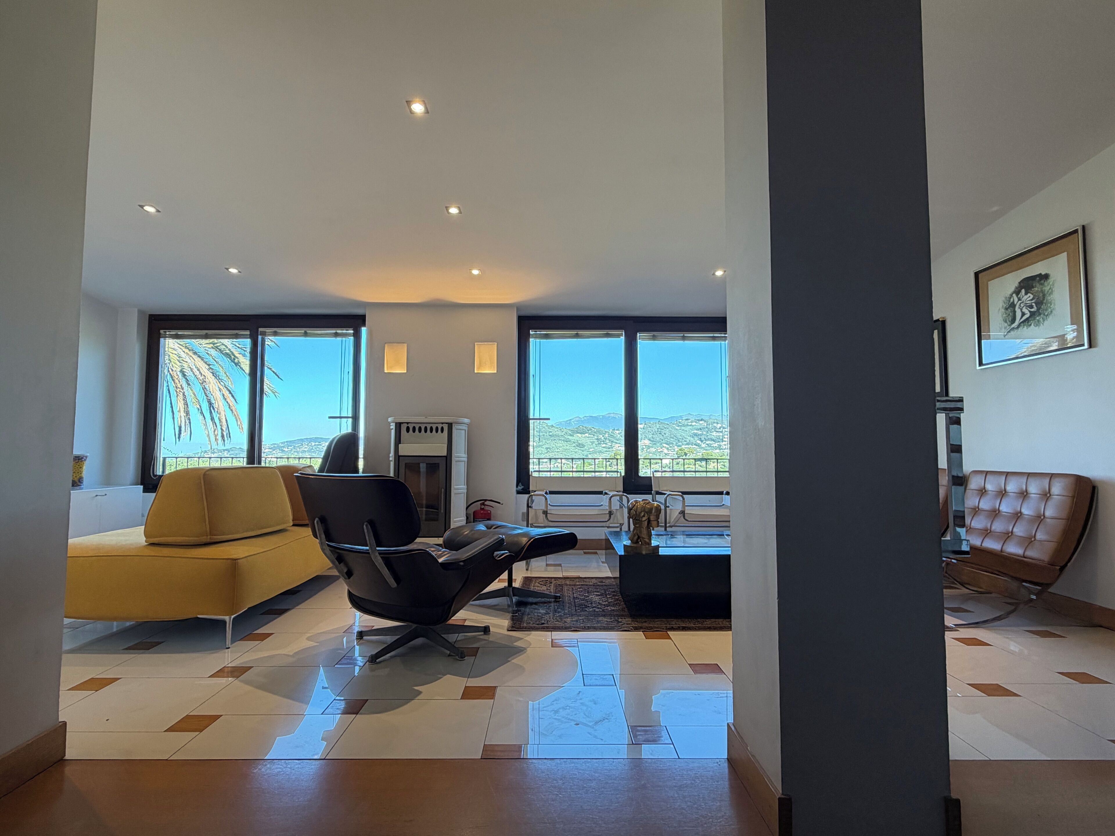 A modern living room with a sofa, a black chair, and a coffee table. There are large windows with a view of the landscape.