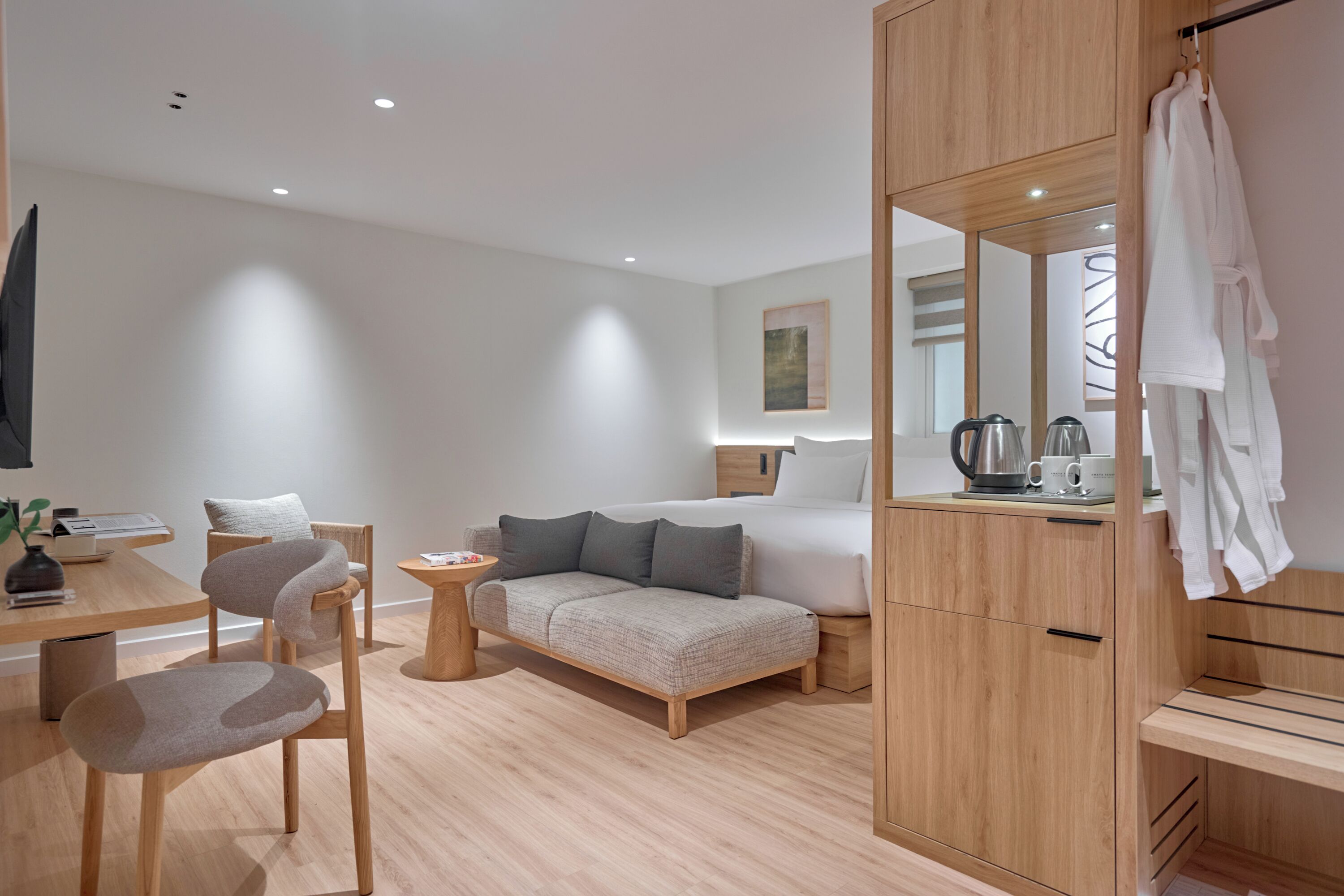 A modern hotel room with a bed, a sofa, a dining area with a table and chairs, a small side table, a mirror, and a wardrobe.