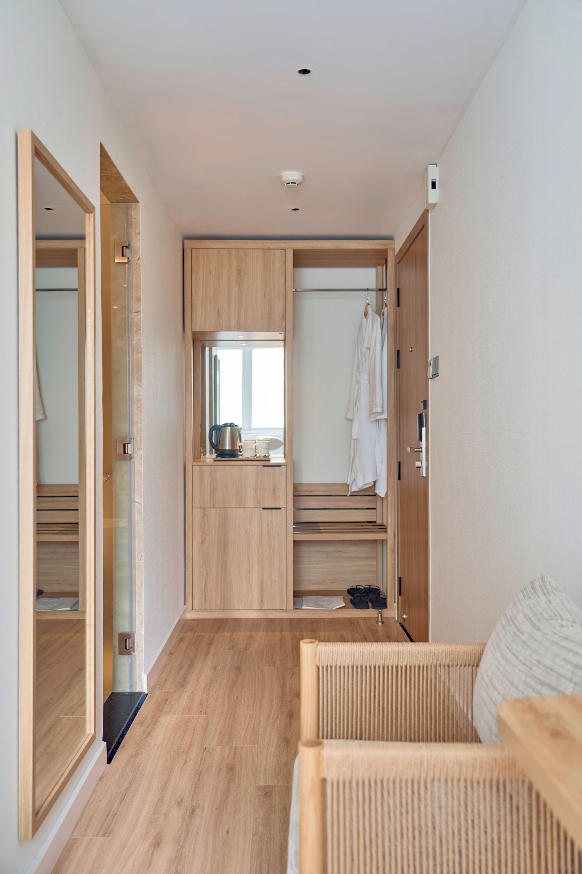 A modern, compact room with a wooden floor, a built-in wardrobe, a mirror, and a seating area with a cushion.