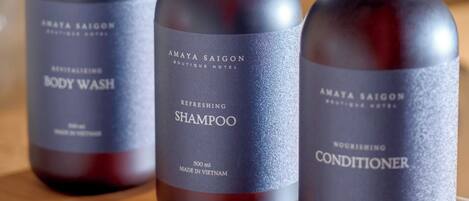 Tres botellas de gel de baño, champú y acondicionador Amaya Saigon sobre una superficie de madera.