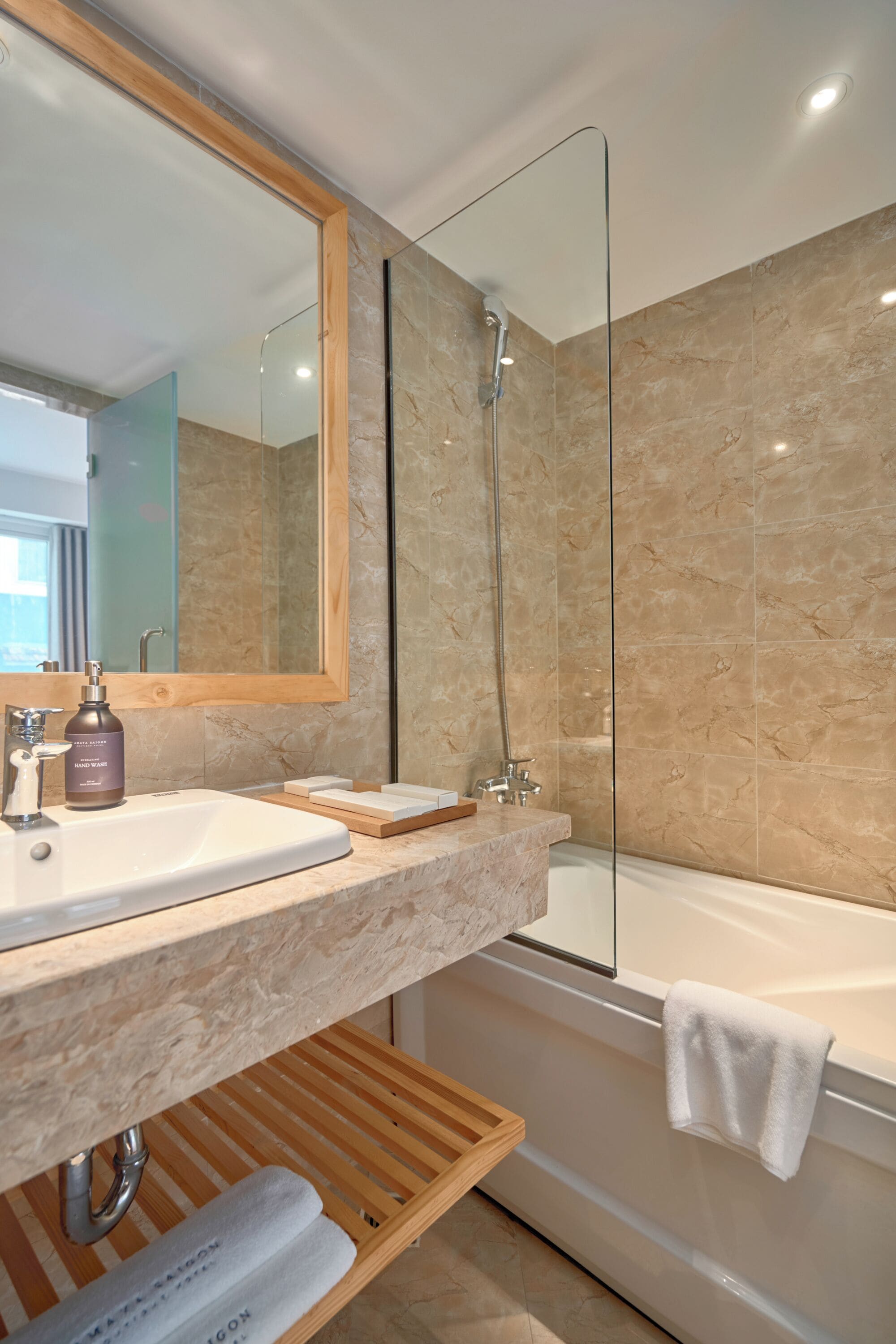 Un baño moderno con lavamanos de mármol, cabina de ducha con mampara de vidrio y bañera blanca.