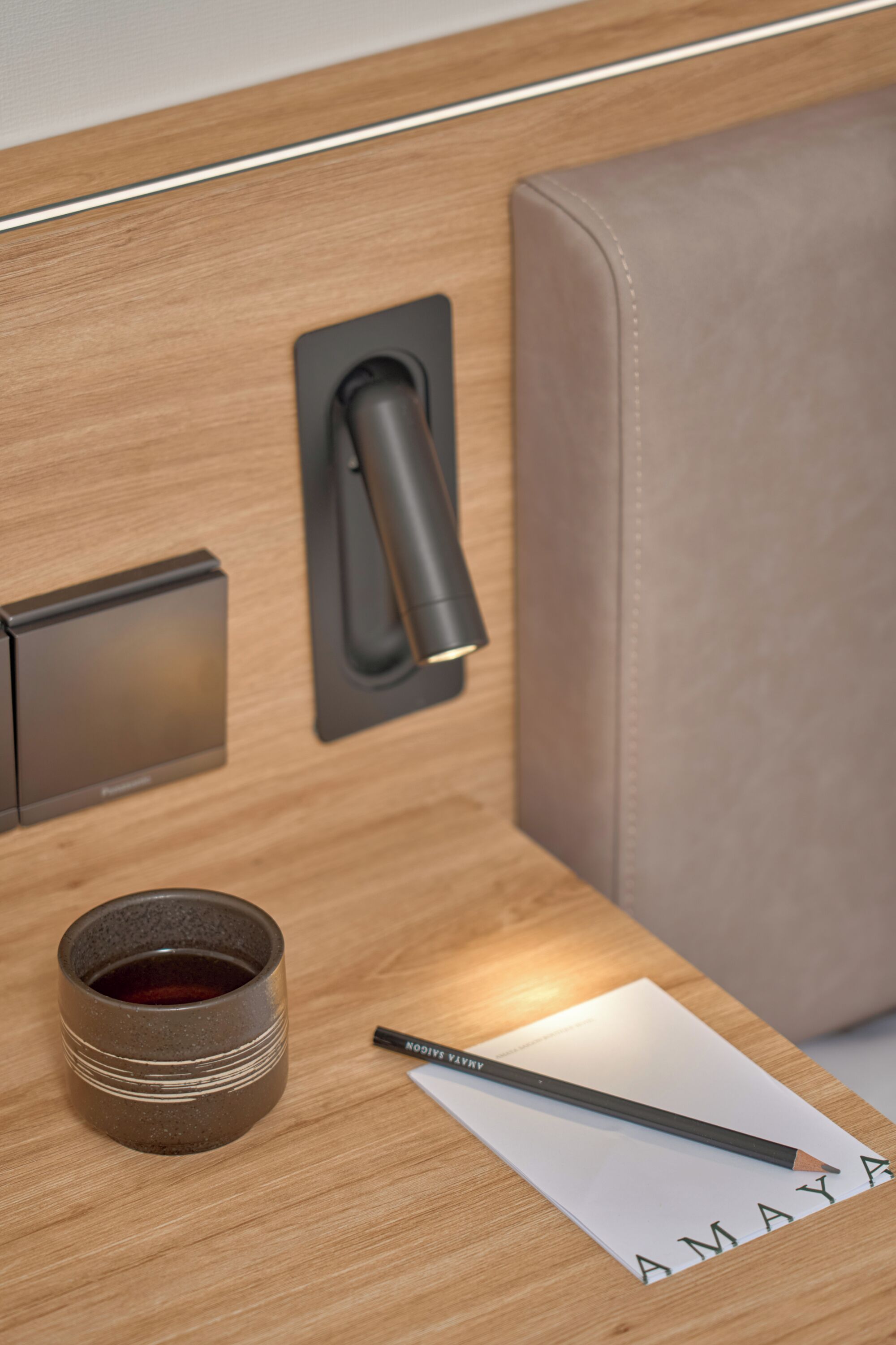 A modern, minimalist room with a wooden panel wall, a black switch, a small cup, a pencil, and a piece of paper with the word "AMAYA" written on it.