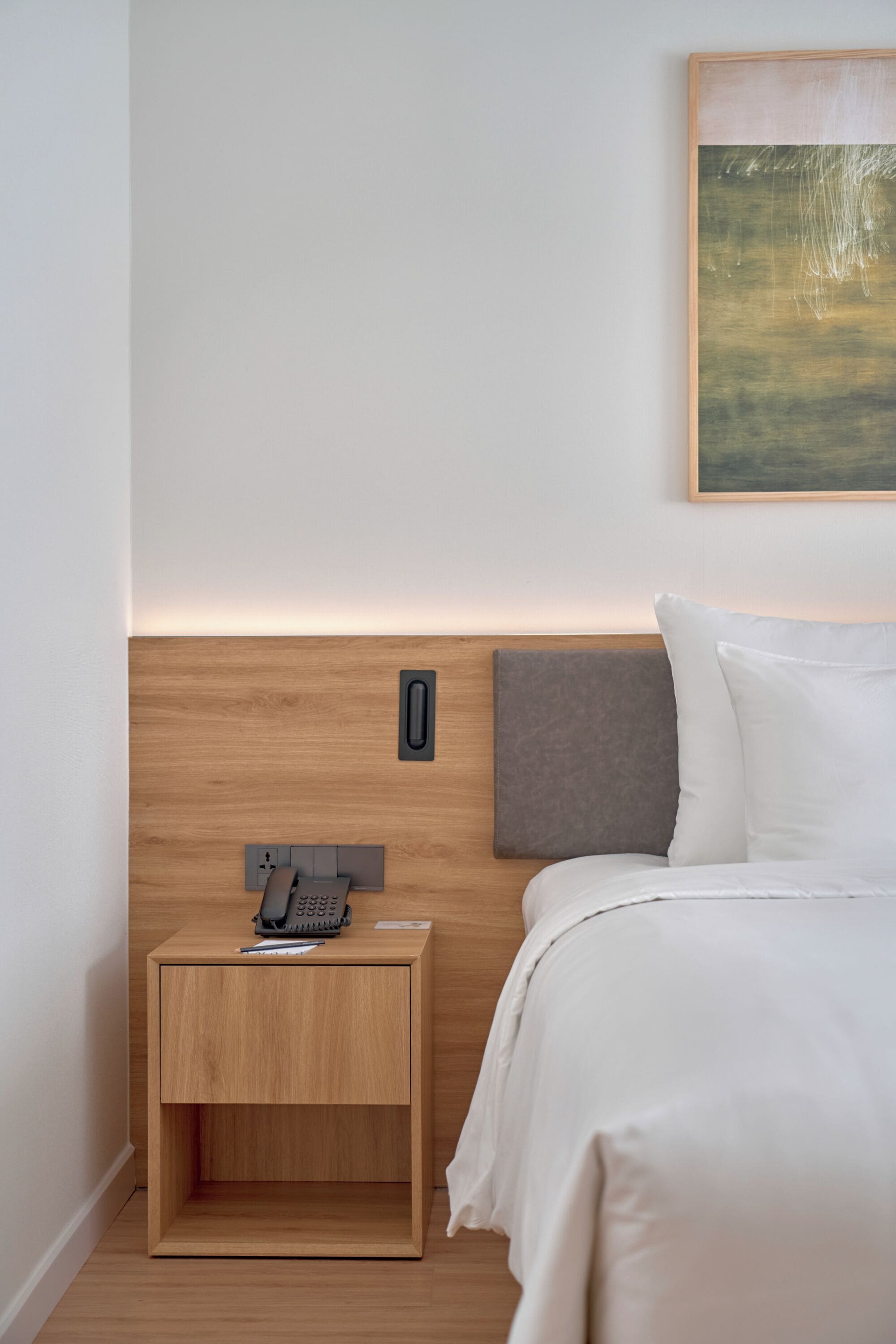 Habitación de hotel con cabecera de madera, mesita de noche con teléfono y un cuadro en la pared.