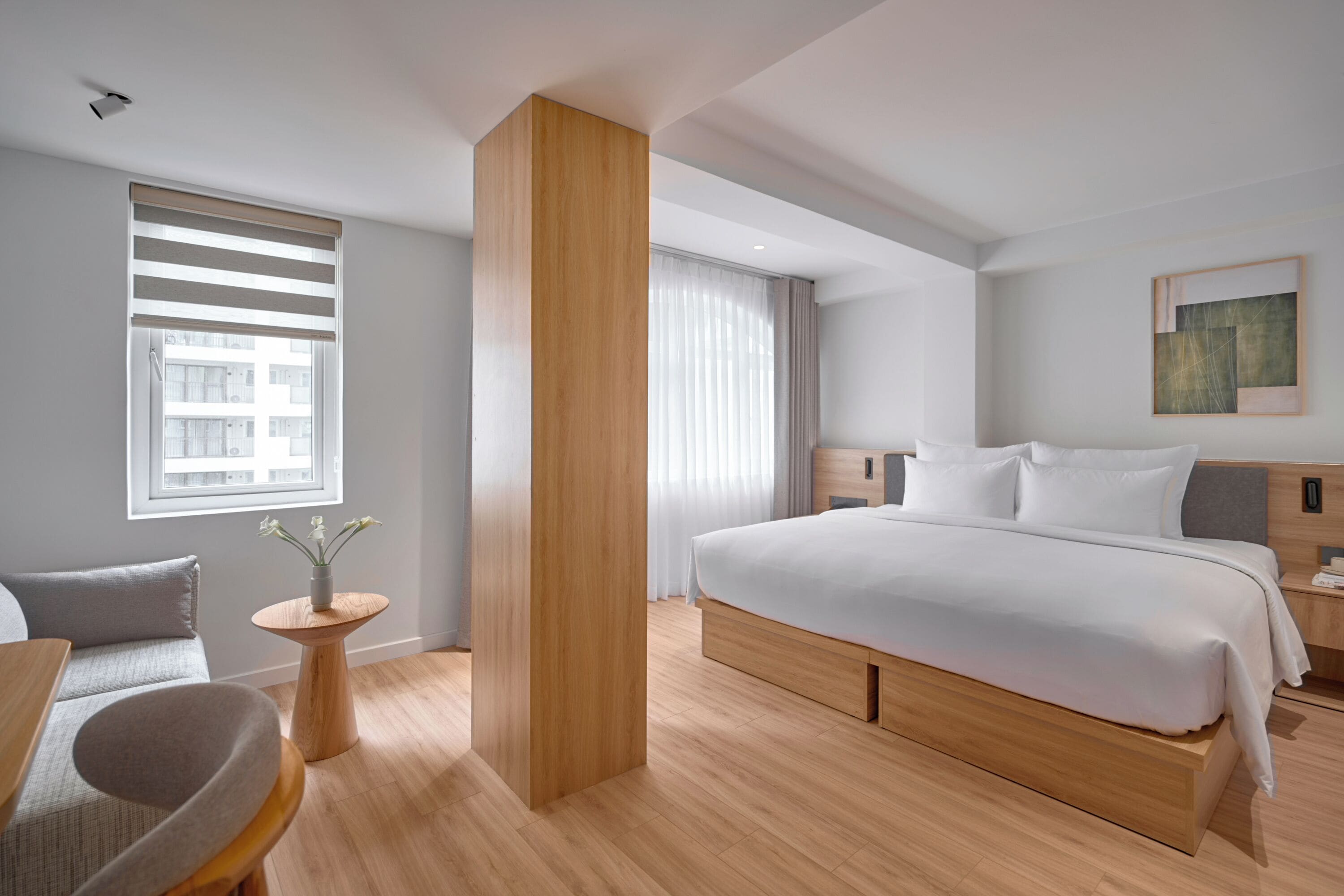 Una habitación de hotel moderna con una cama grande, un cabecero de madera, una mesita de noche, una silla y una pequeña mesa con un florero.