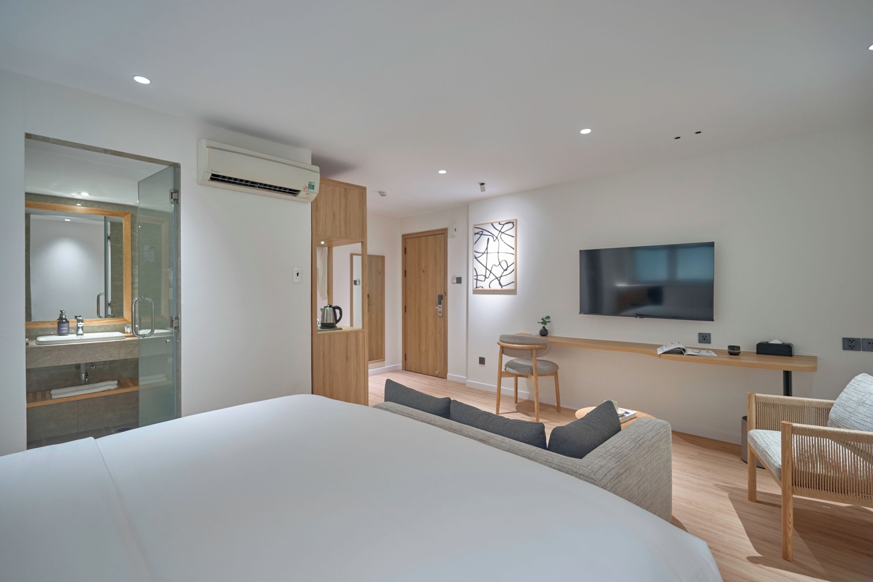 A modern hotel room with a large bed, a TV, a desk, and a seating area.