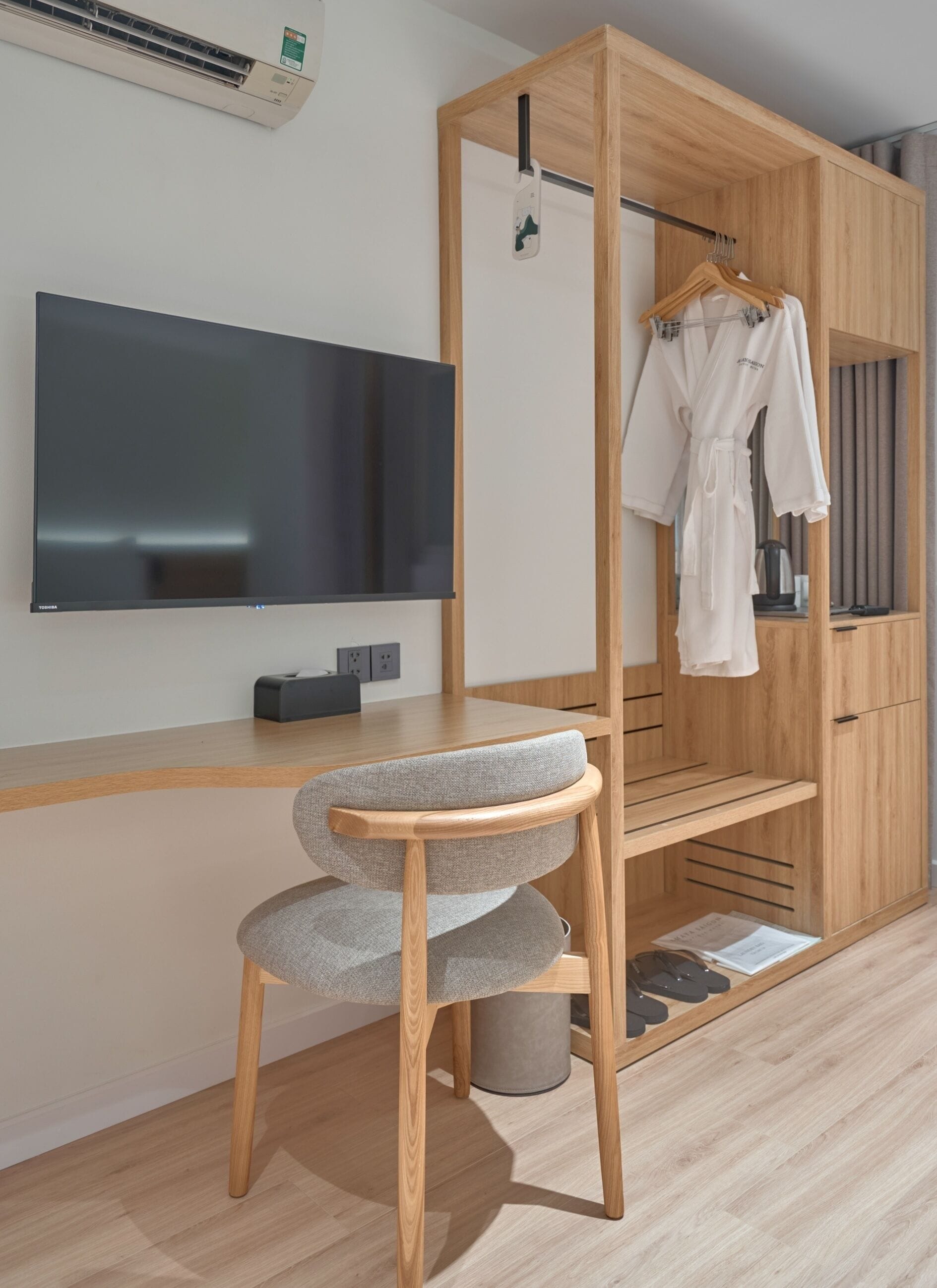 A modern room with a wooden wardrobe, a grey upholstered chair, a flat-screen TV, and a hanging robe.