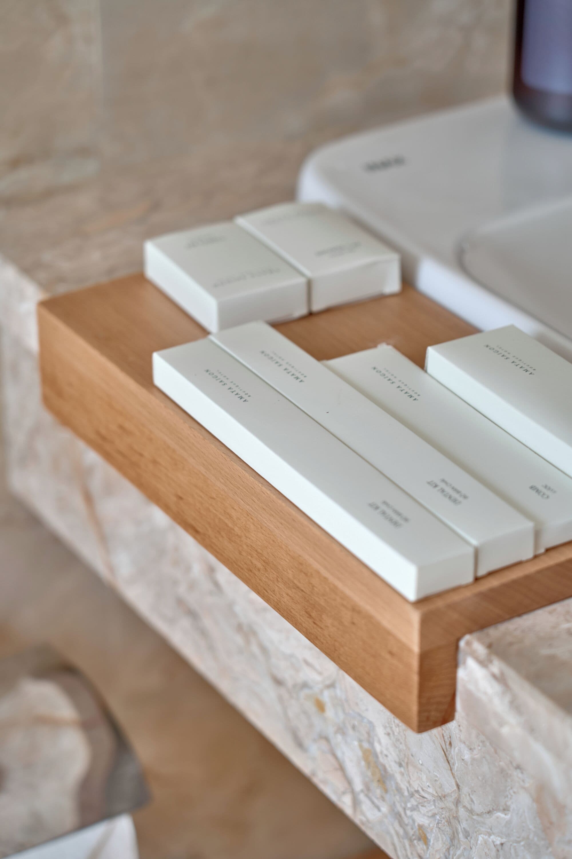 Une étagère en bois, sur laquelle sont posées plusieurs boîtes blanches, probablement contenant des articles de toilette ou des produits d’accueil, le tout adossé à un mur en pierre.