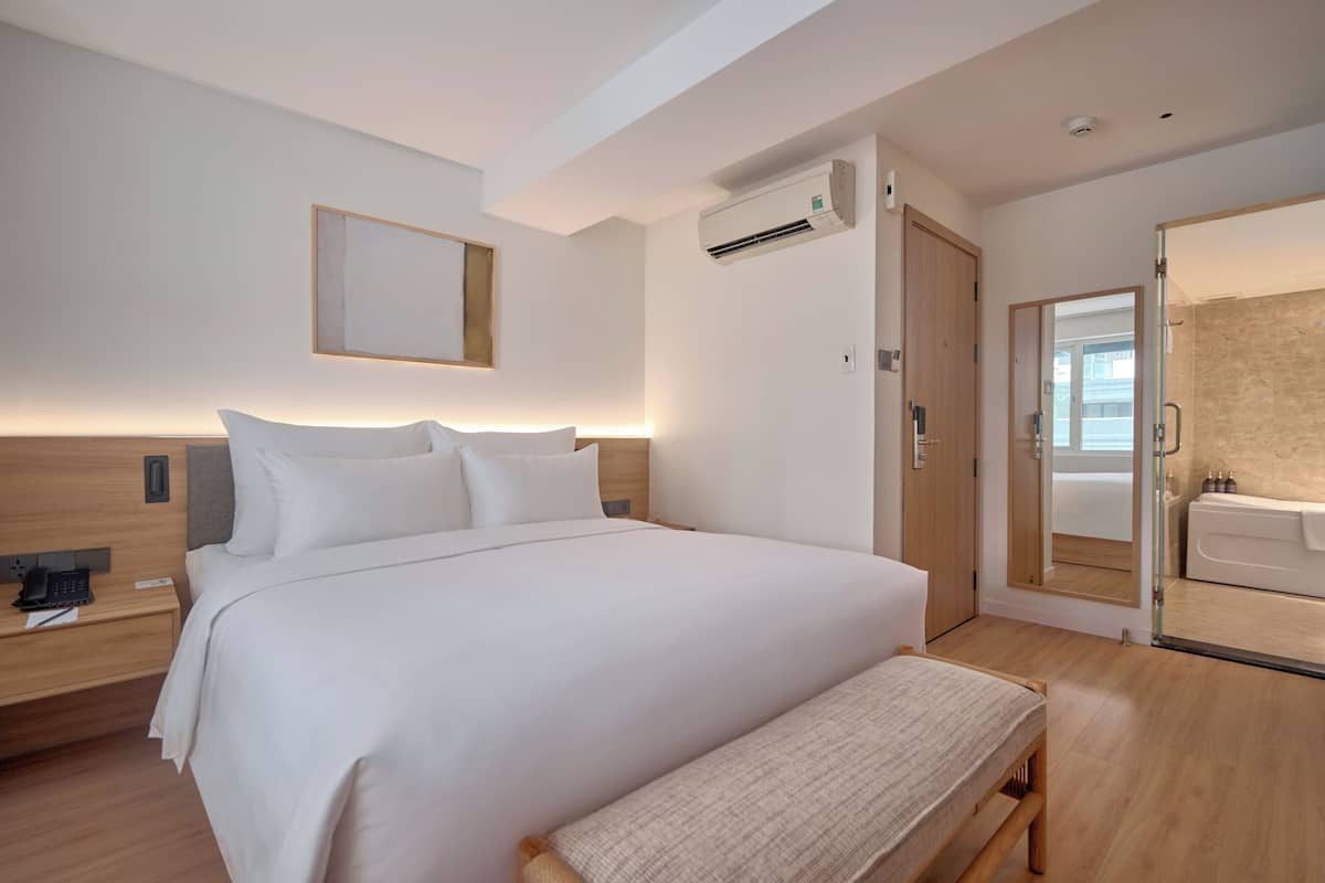 A modern hotel room with a large bed, bedside table, and a bathroom with a bathtub and shower.