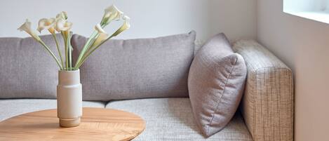 A modern living room with a grey sofa, a round wooden coffee table, and a vase with flowers.