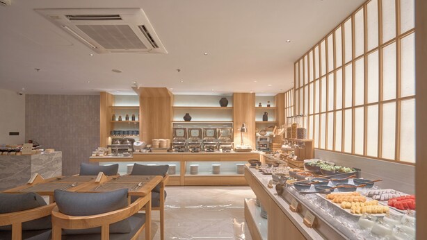 A modern dining area with wooden furniture and a buffet counter with various food items. - Amaya Saigon Boutique Hotel (Ho Chi Minh City)