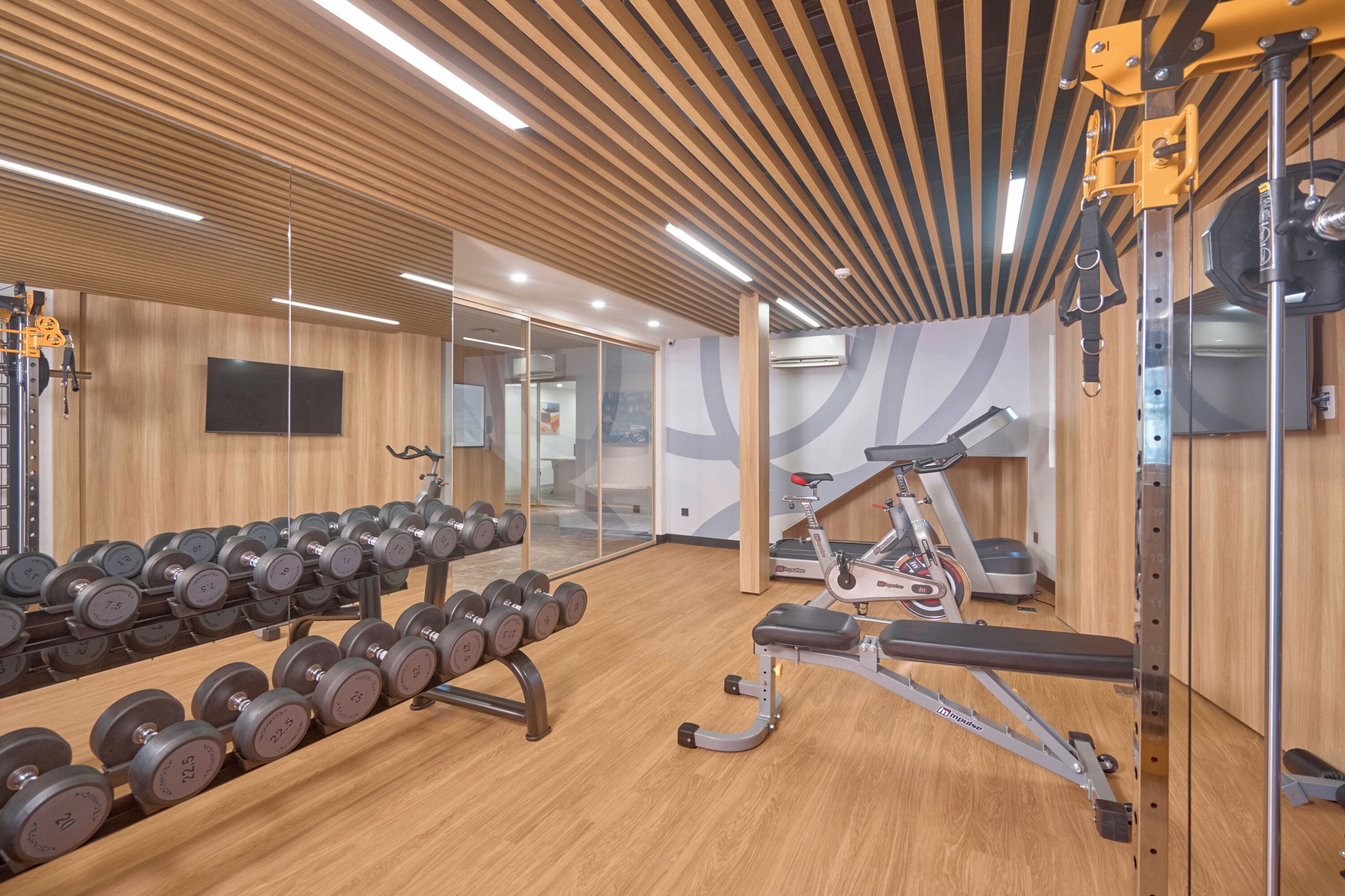 A gym with wooden floors, exercise equipment, and a large mirror.