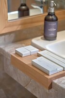 A bathroom with a marble countertop, a wooden shelf with boxes, and a bottle of hand soap.