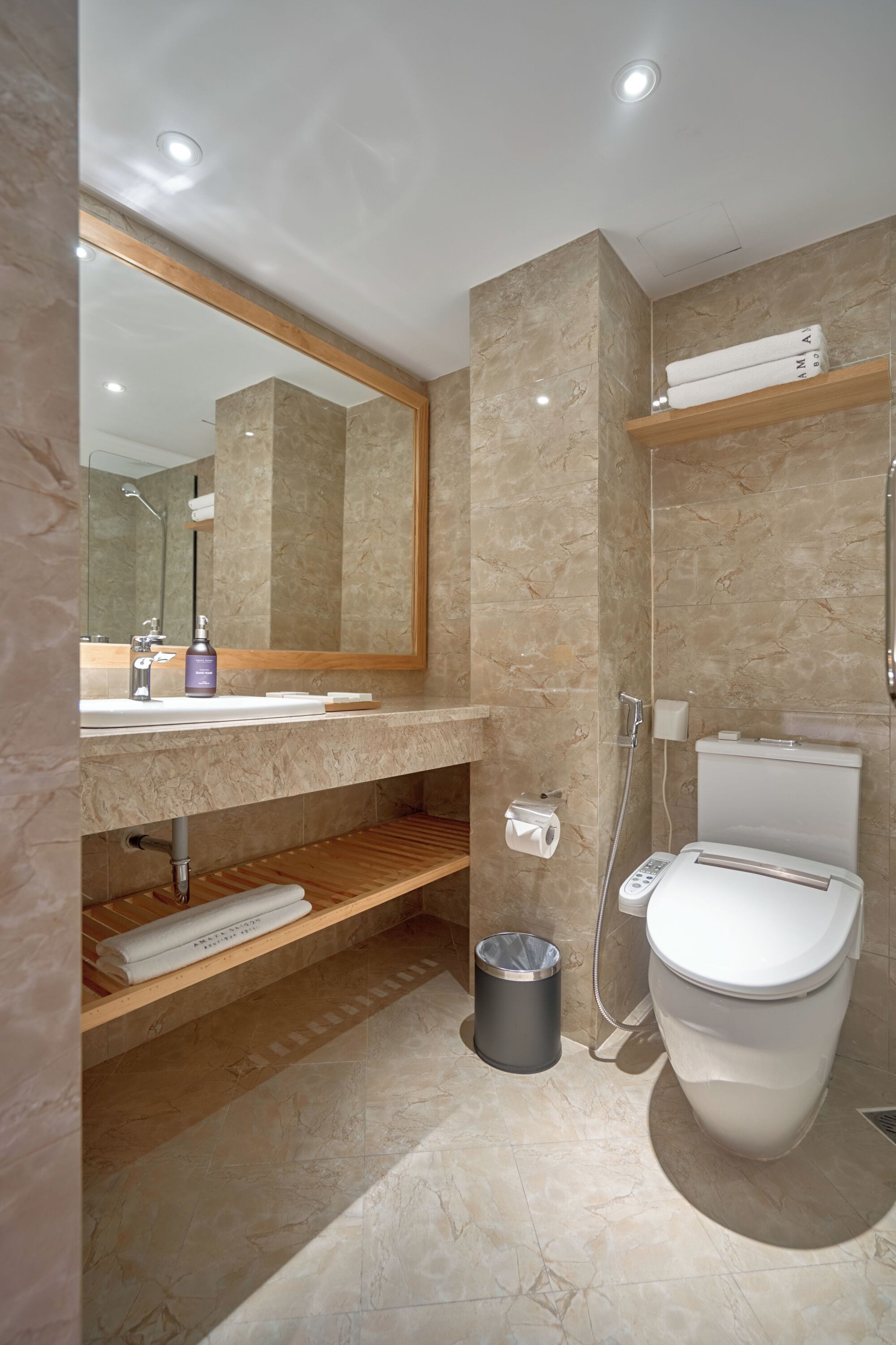 A modern bathroom with a marble sink, a large mirror, a toilet, and a shower.