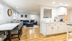 A modern kitchen with white cabinets, a black faucet, and a marble countertop. There is a dining area with a white table and chairs, and a gray sofa in the background. - Charming Coastal Retreat w Community Beach Dog-Friendly & Mins to Downtown Annapolis (Annapolis)