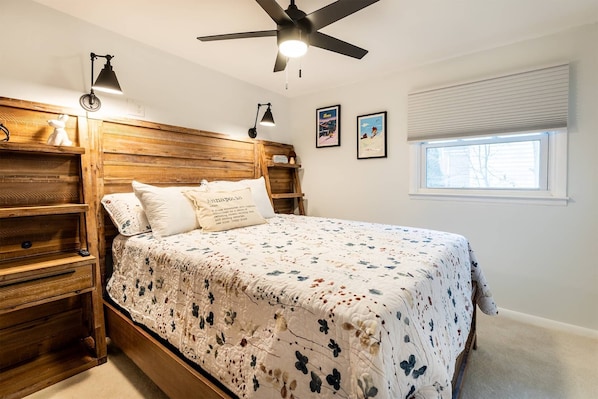 A bedroom with a wooden headboard, a bed with a floral bedspread, two wall-mounted reading lamps, and a ceiling fan.