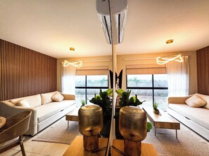 A modern living room with a sofa set, a coffee table, and a large window providing a view of greenery. - Indigo 7, Steps from Playa Brujas Beach (Mazatlán)