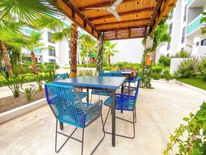 Une terrasse extérieure avec une table et des chaises, entourée de verdure et de palmiers.