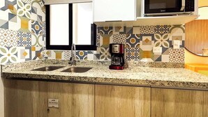 Une cuisine dotée d’un plan de travail en granit, d’un évier en acier inoxydable, d’une machine à café, d’un four à micro-ondes et de carreaux décoratifs sur le mur derrière l’évier.