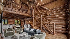 L’intérieur d’une cabane en rondins, avec un coin repas, un canapé et un escalier.