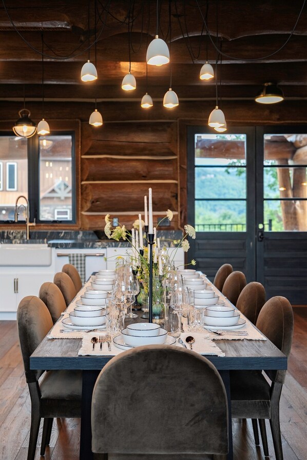 Una larga mesa de comedor dispuesta para seis personas, con una mesa de madera rústica, sillas de terciopelo y un centro de mesa con velas y flores.