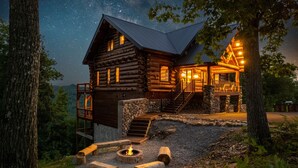 Une cabane en rondins avec des fondations en pierre, une terrasse en bois et un foyer extérieur.