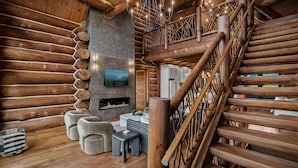L’intérieur d’une cabane en rondins, avec un escalier en bois, une cheminée et un téléviseur fixé au mur.