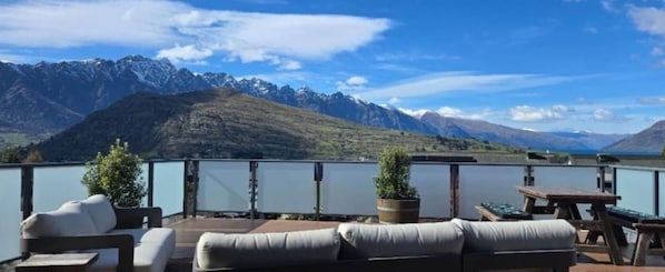 A terrace with outdoor seating, a view of mountains, and a body of water.