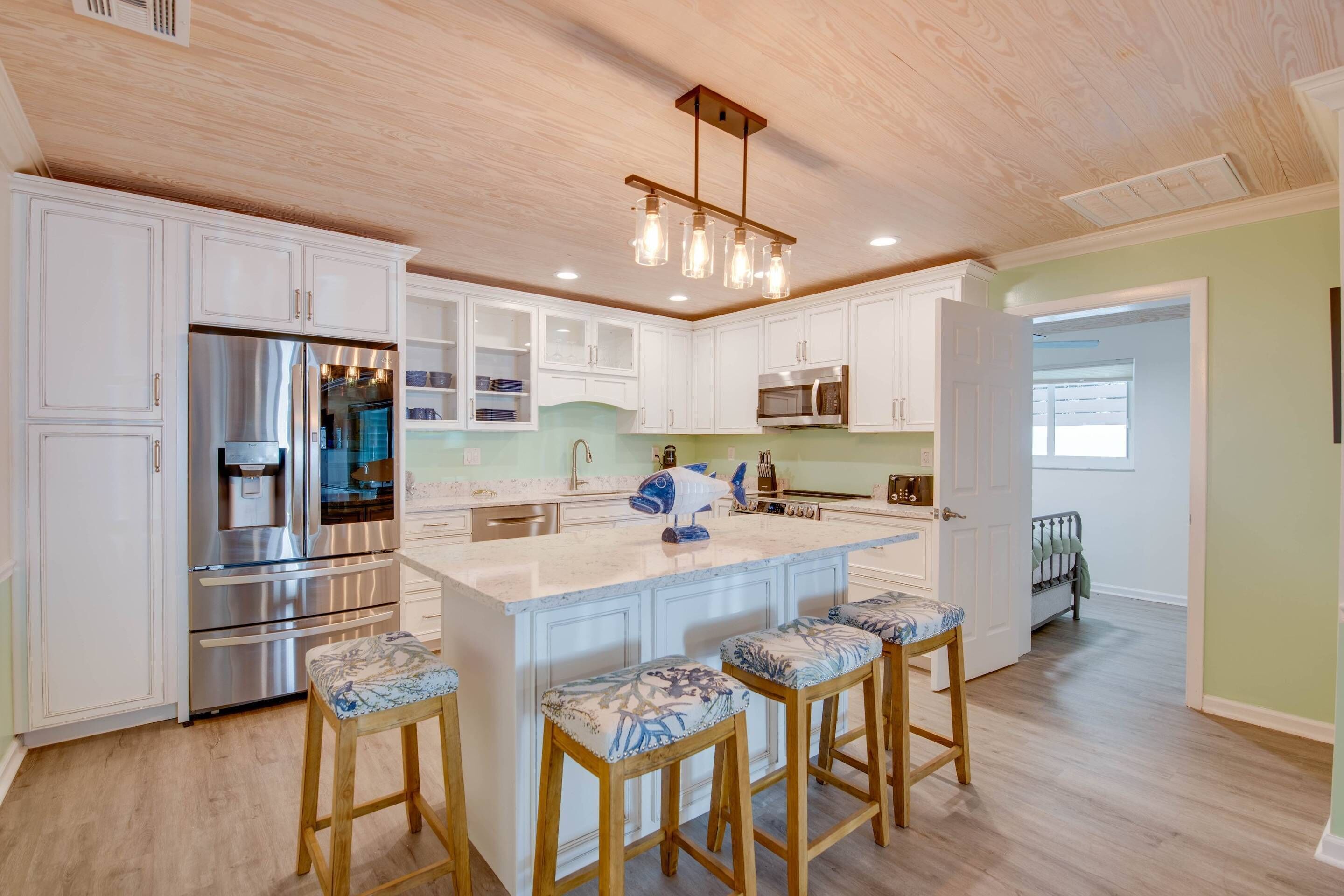 A modern kitchen with white cabinetry, stainless steel appliances, and a central island with bar stools.