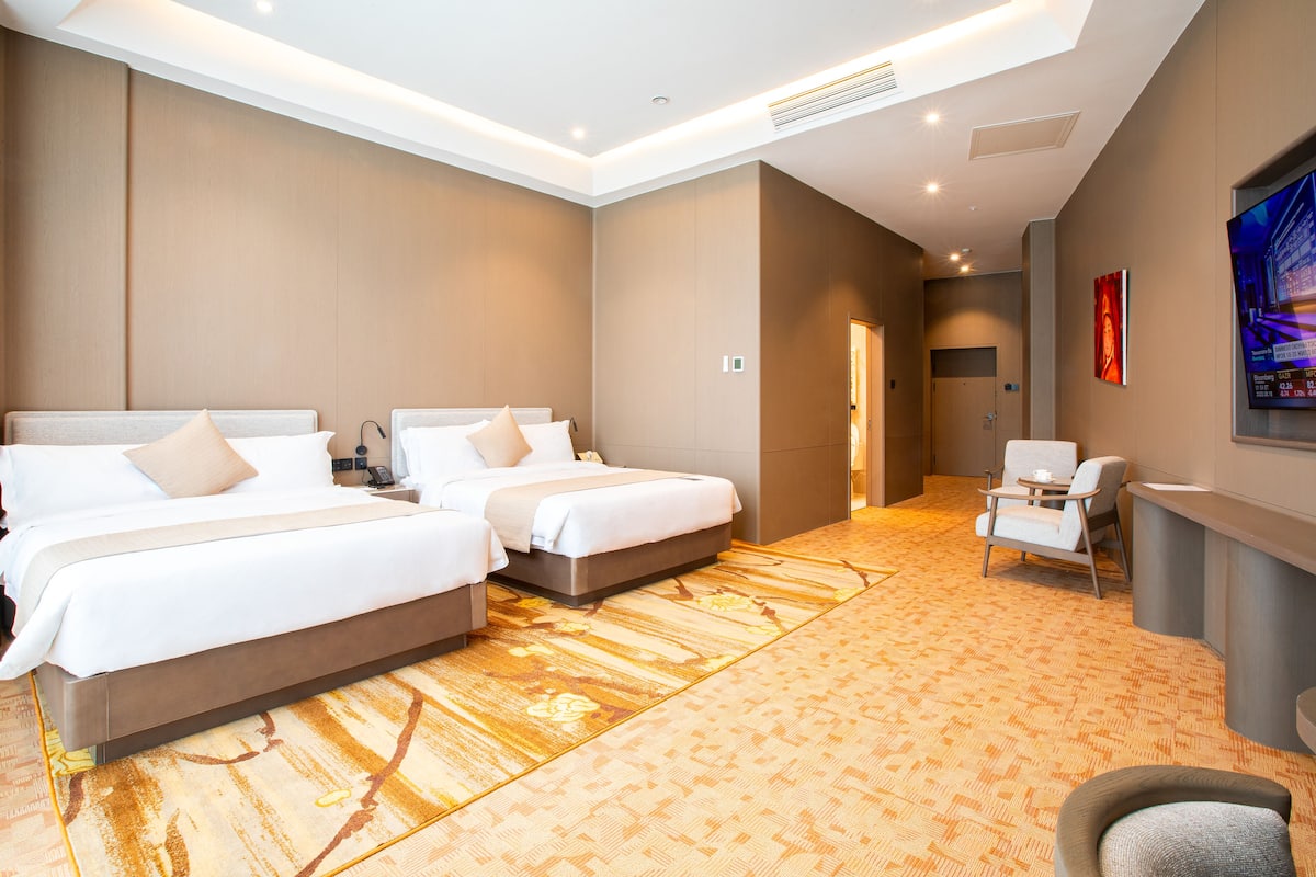 A hotel room with two beds, a desk, a chair, and a television.